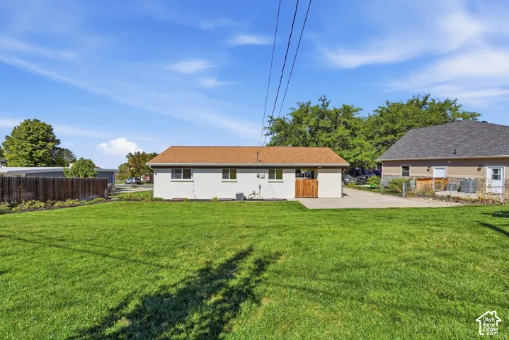 Expansive green lawn, wood fence, concrete driveway, and a tan exterior with a brown roof