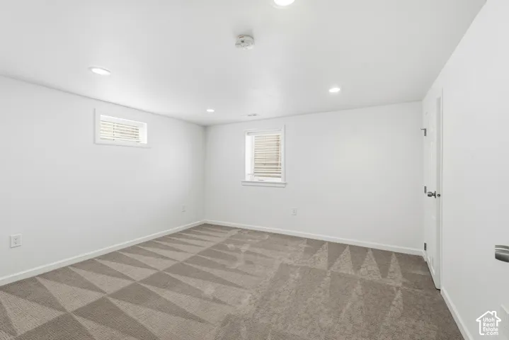 Recessed lighting, light-colored walls, patterned carpet, and two windows with blinds