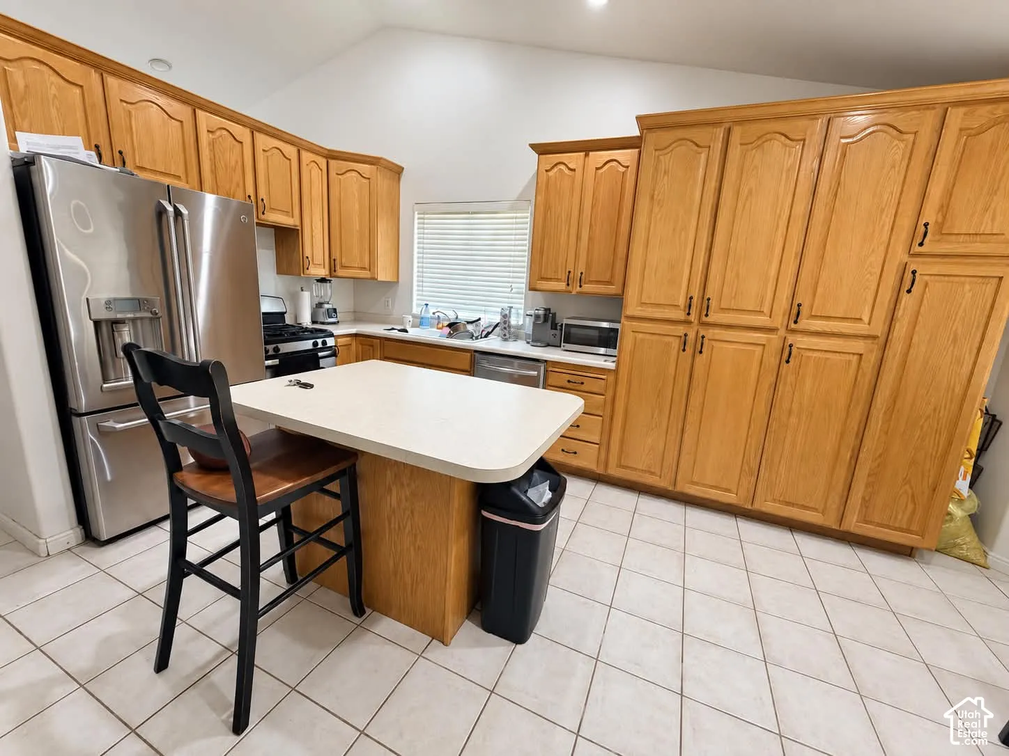 Kitchen with wood-finish cabinetry, stainless steel refrigerator, white countertops, a central island, and tiled flooring
