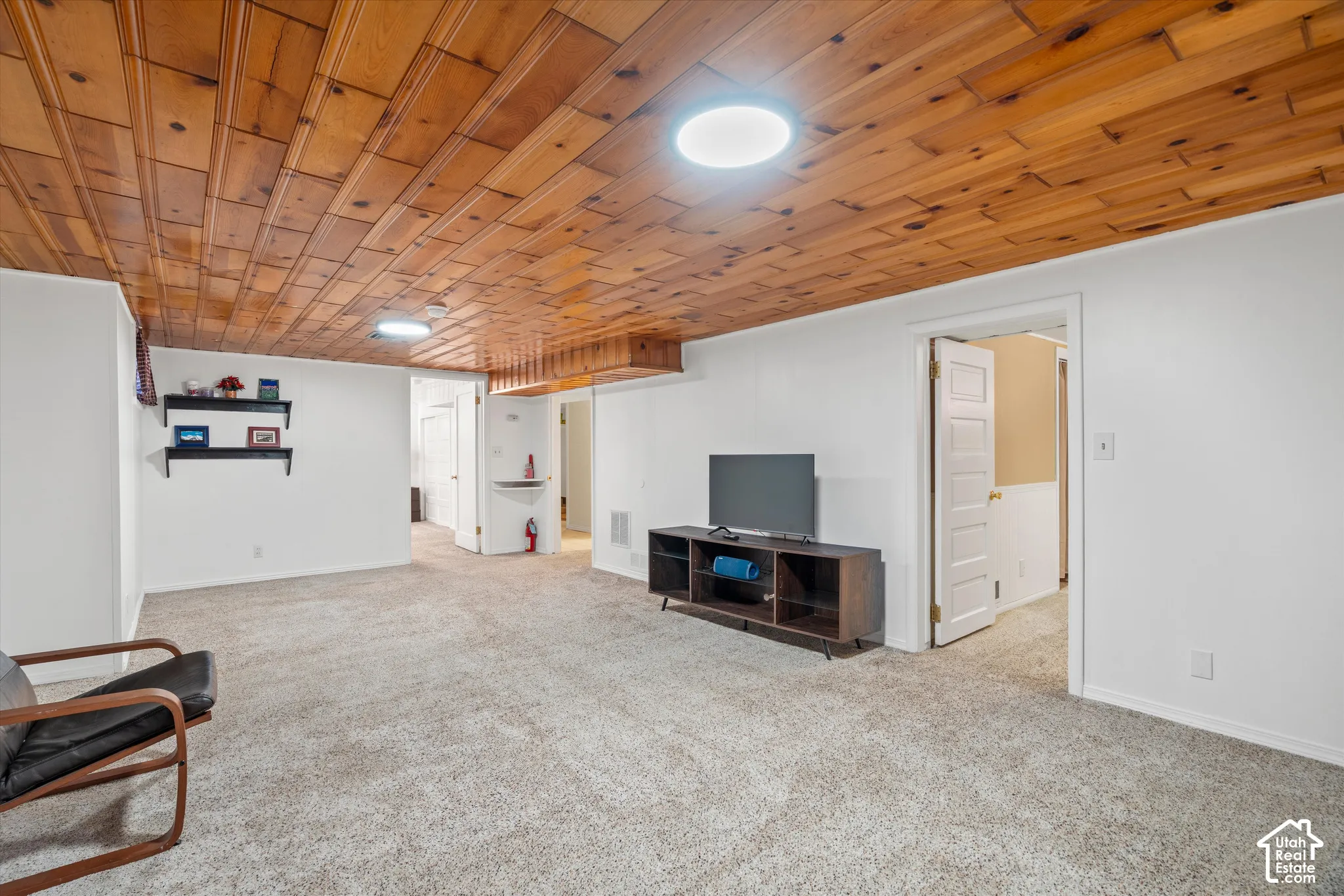 Recessed lighting illuminating a wood-panel ceiling, neutral carpeting, white wall finishes, and interior doors with panel details