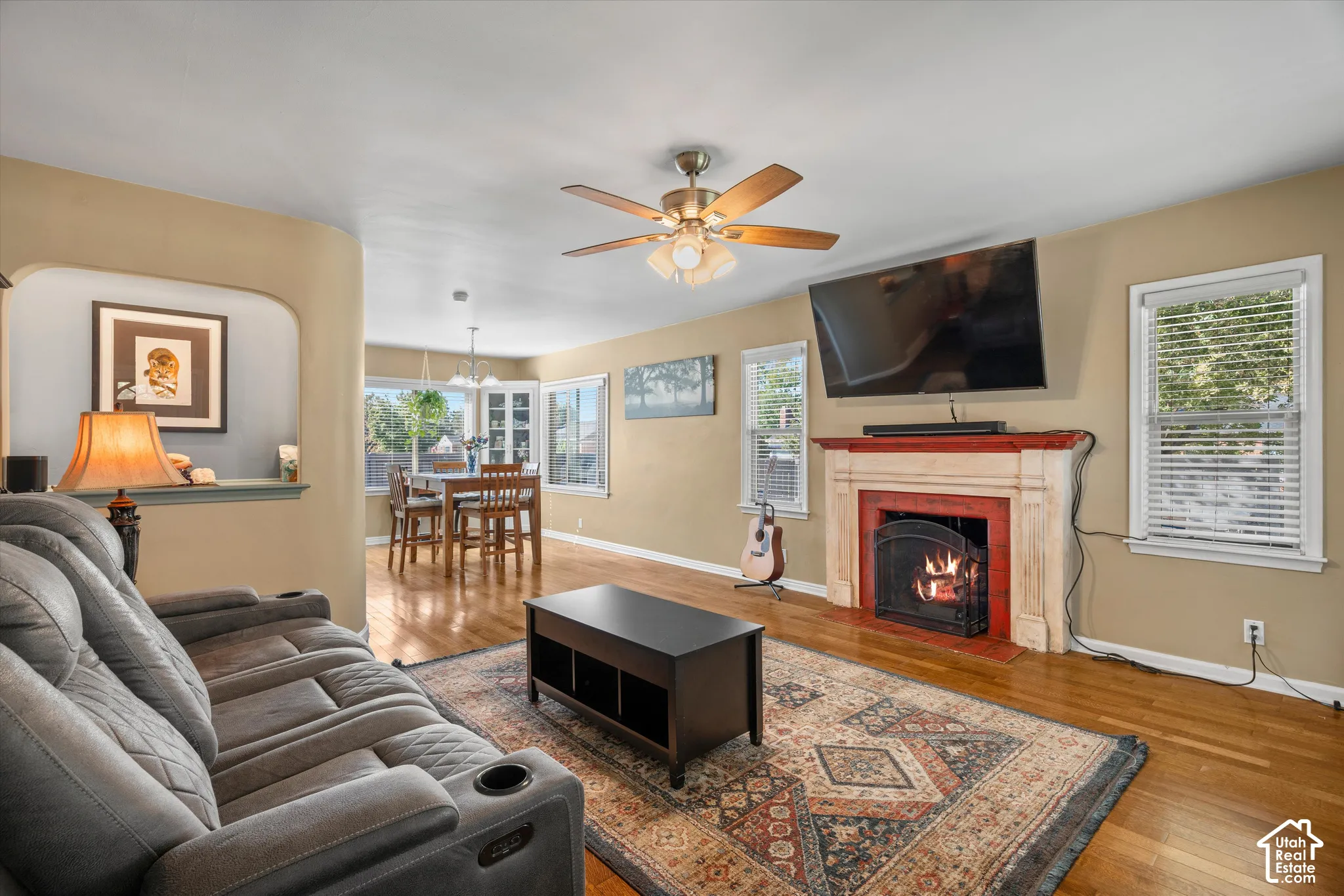 Hardwood flooring throughout, a ceiling fan with integrated lighting, and a fireplace with a decorative mantel