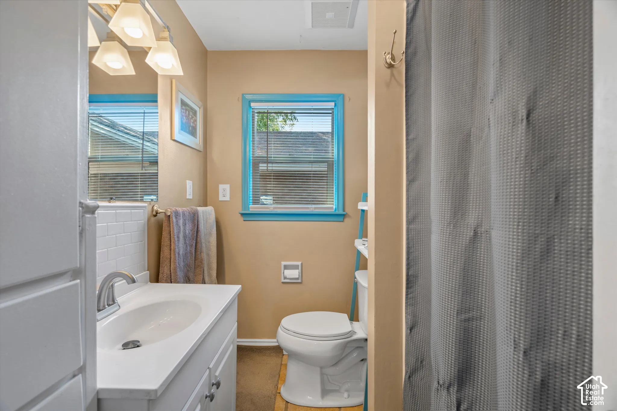 Bathroom featuring a single vanity, undermount sink, brushed nickel faucet, wall-mounted light fixture, and a window with blinds