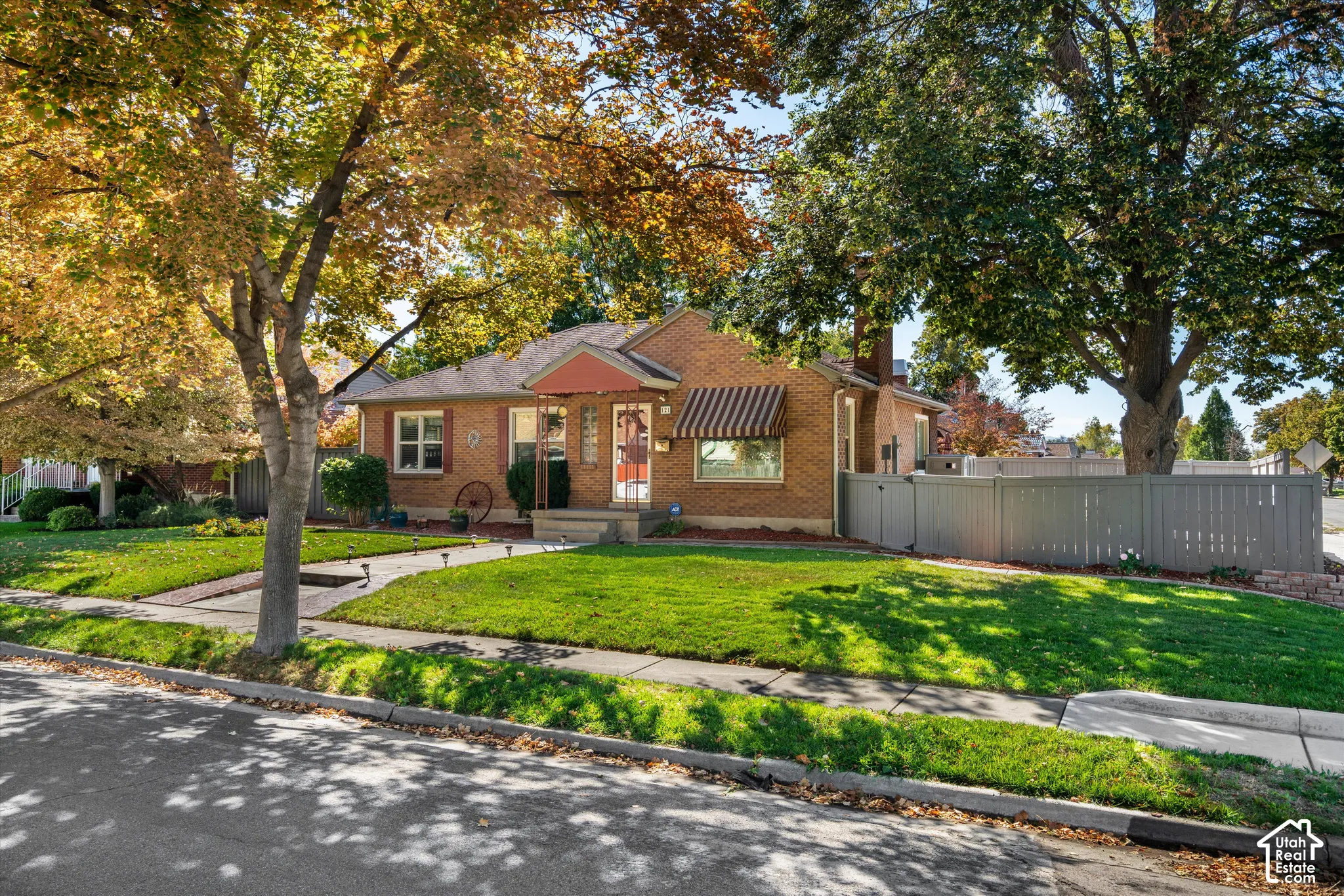 Brick exterior with a covered porch, striped awning, and mature trees