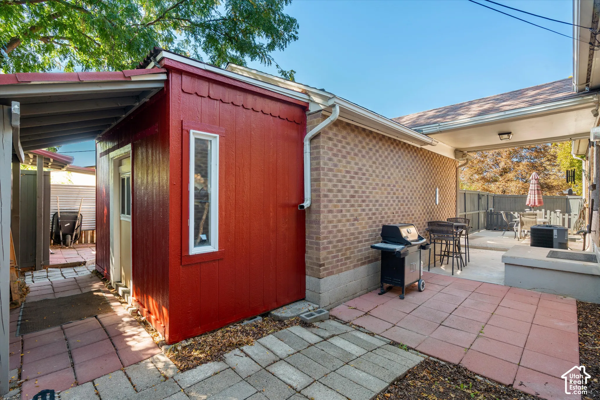 Brick exterior, covered patio, red shingle-sided shed, paver patio, and mature trees