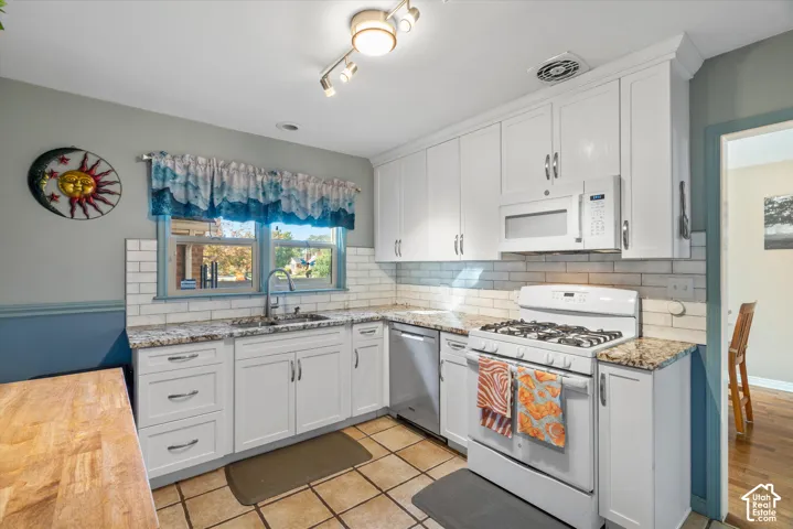 White cabinetry with stainless steel hardware, granite countertops, subway tile backsplash, built-in microwave, and a window with natural light