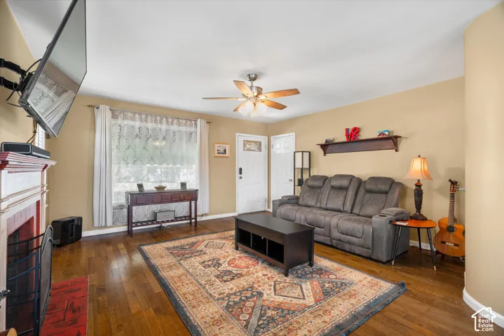 Hardwood-finish flooring, ceiling fan with integrated lighting, built-in wall shelf, and a fireplace with a decorative mantel