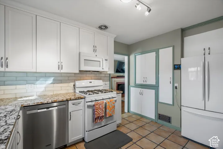 White cabinetry, natural stone countertops, subway tile backsplash, stainless steel dishwasher, and track lighting