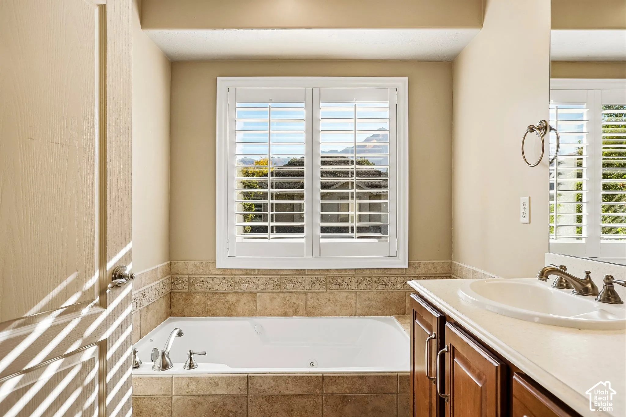 Integrated soaking tub, plantation shutters, vanity with double-door cabinetry, countertop with integrated sink, and bronze-finish hardware