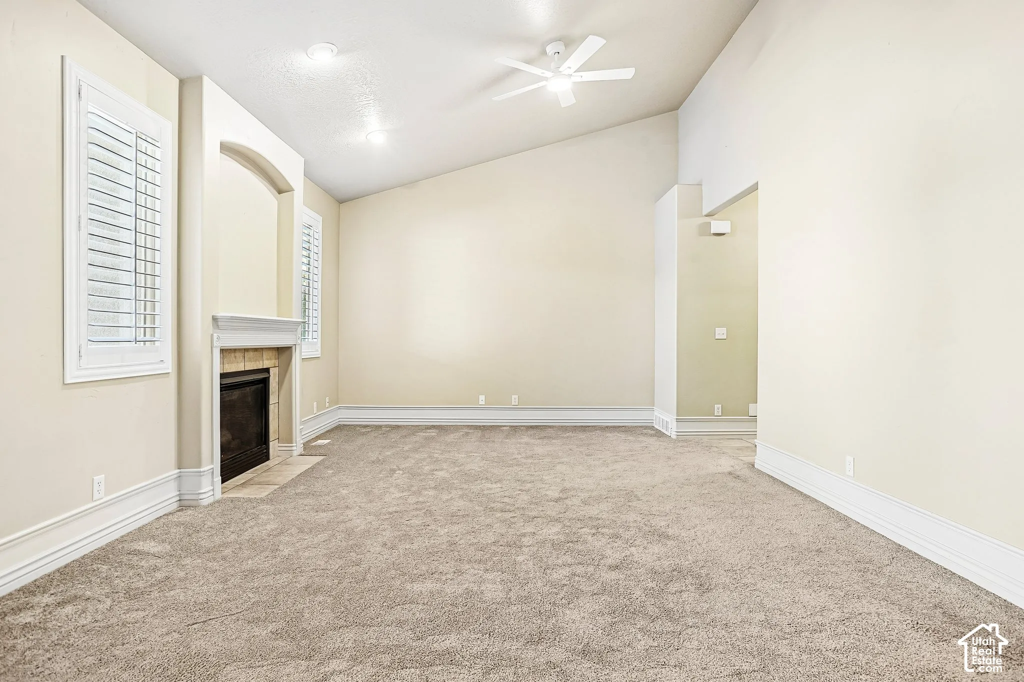Vaulted ceiling with a ceiling fan, recessed lighting, fireplace with a mantel, plantation shutters, and carpet flooring