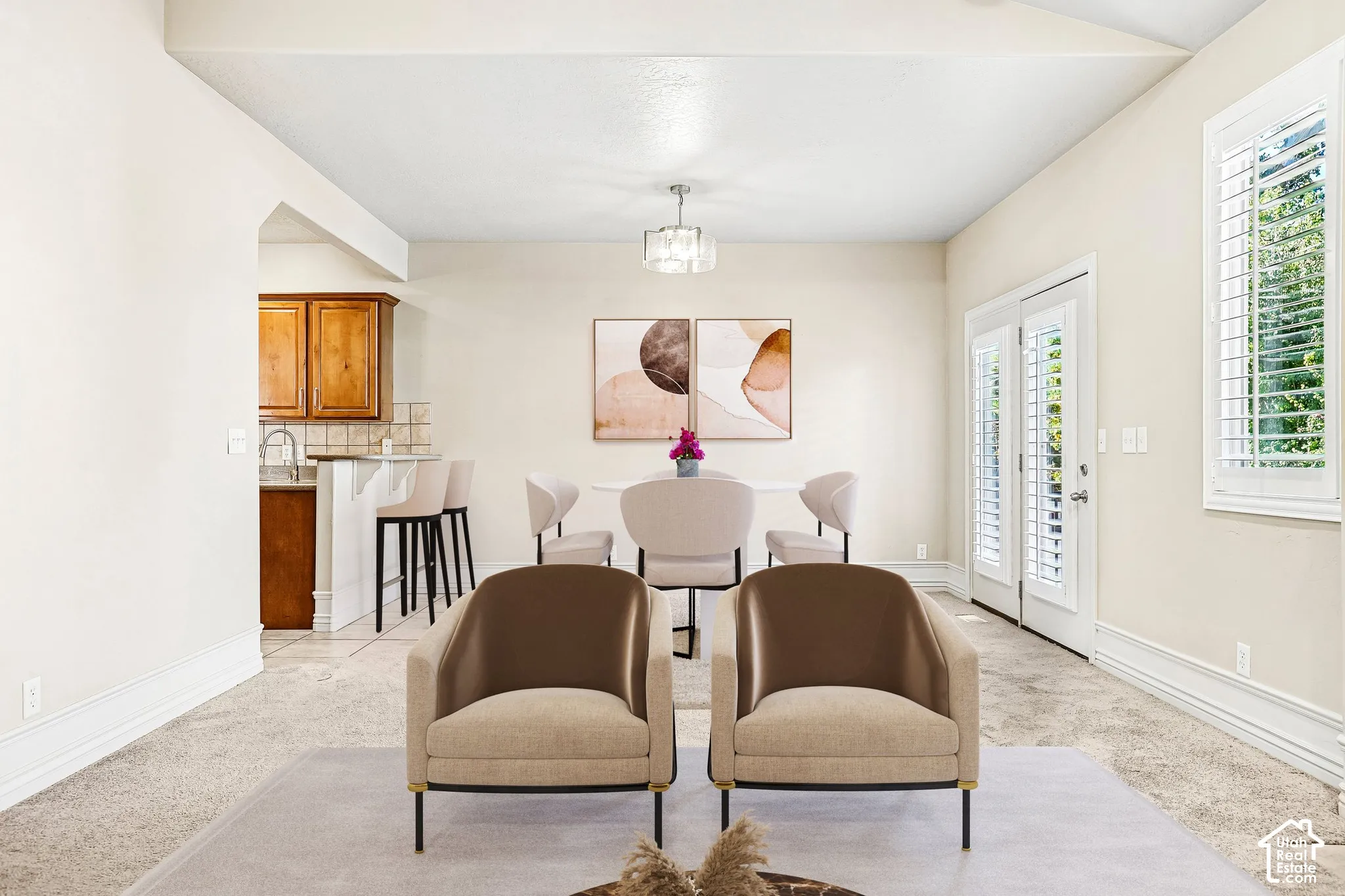 Vaulted ceiling with a contemporary chandelier, French doors with interior shutters, wall-to-wall carpeting, and wood cabinetry in the kitchen area