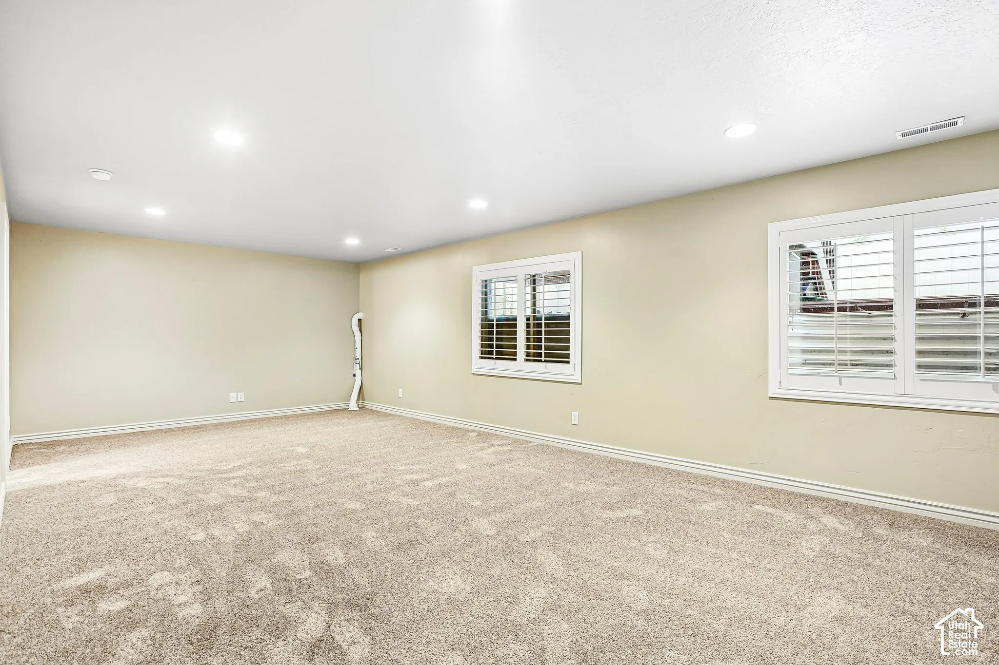 Expansive carpeted room featuring recessed lighting and two windows with white plantation shutters