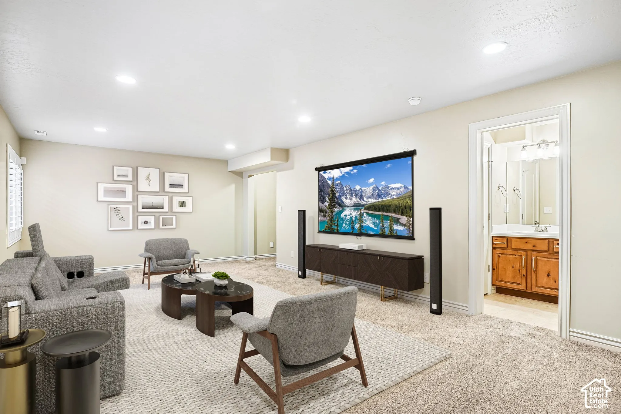 Recessed lighting illuminates this carpeted living area, featuring an entertainment screen and a wood-finish media console