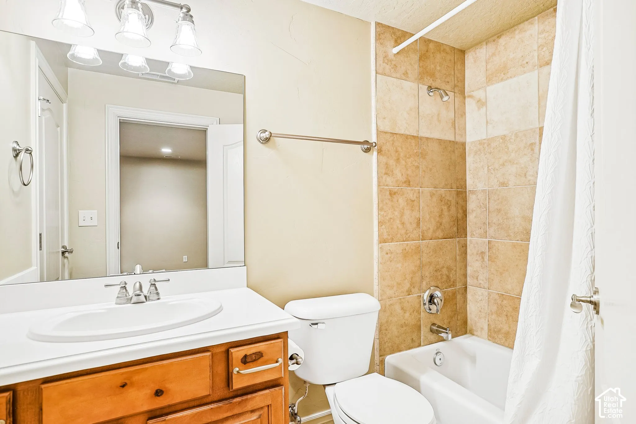 Bathroom featuring a wood-finish vanity, white countertop, integrated sink, and a shower/tub combination with tiled surround