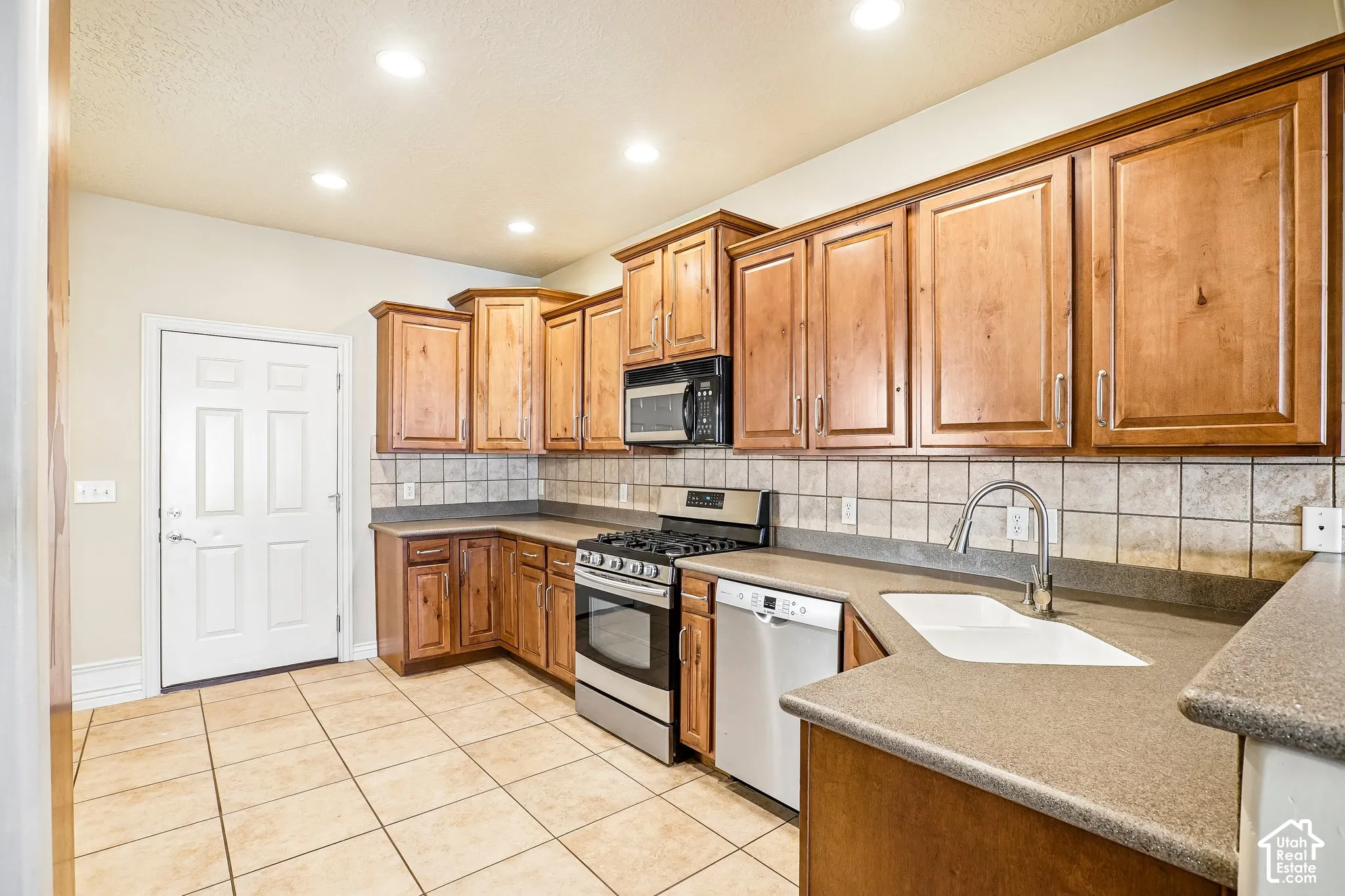U-shaped kitchen with wood cabinetry, stainless steel appliances, tile flooring, and a tile backsplash