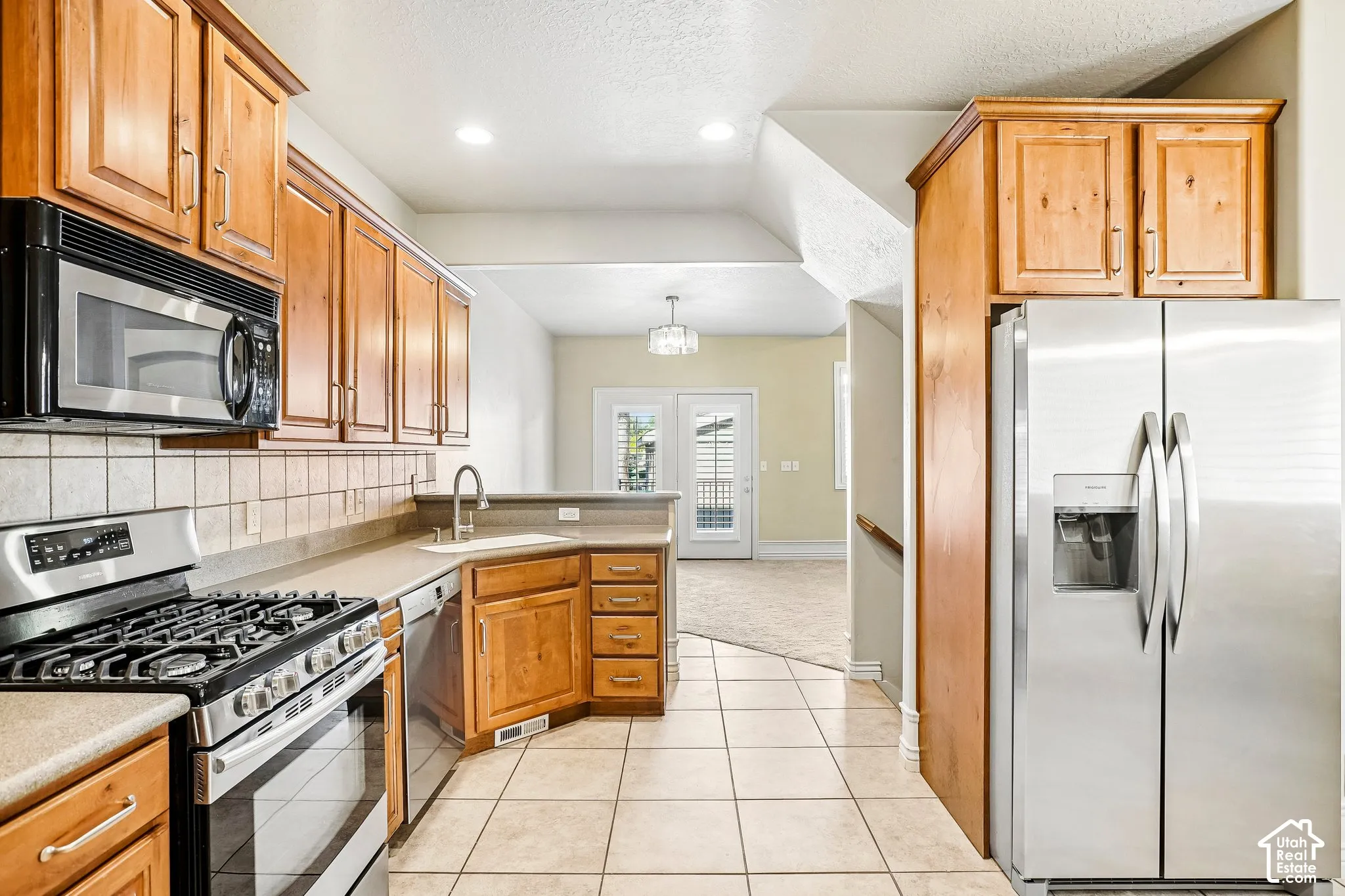 Kitchen featuring stainless steel appliances, wood cabinetry, tile flooring, and a tile backsplash