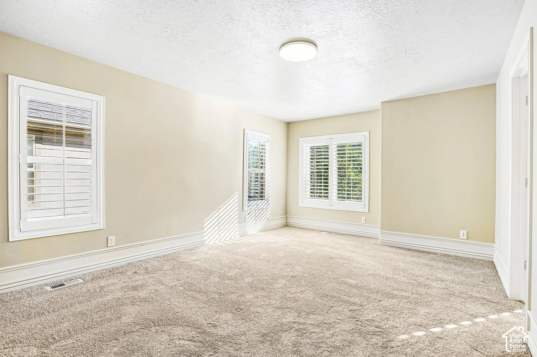 Textured carpeting, multiple windows with plantation shutters, recessed baseboard trim, and a flush mount ceiling light fixture
