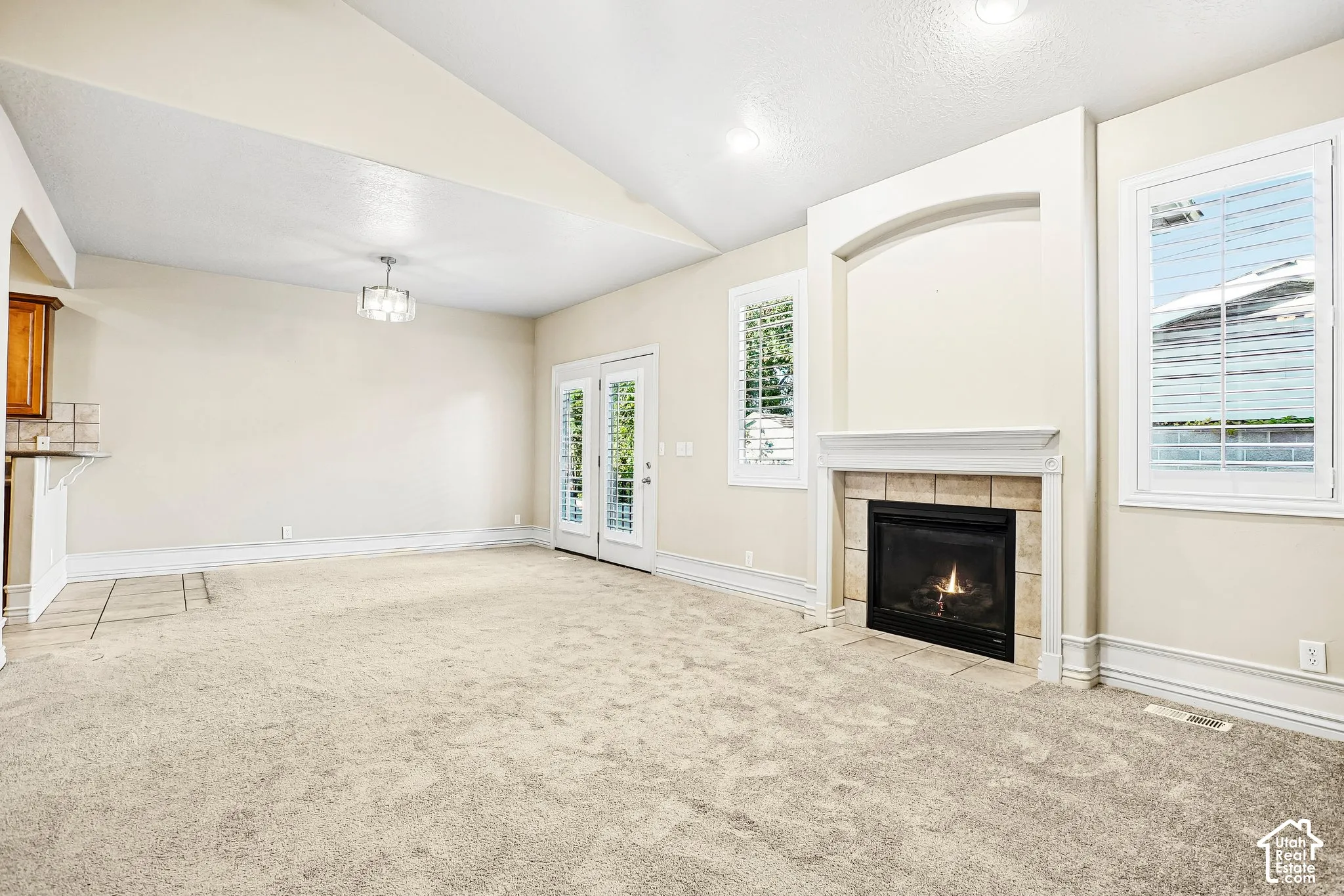 Arch-detailed fireplace with tile surround, French doors, plantation shutters, vaulted ceiling, and recessed lighting