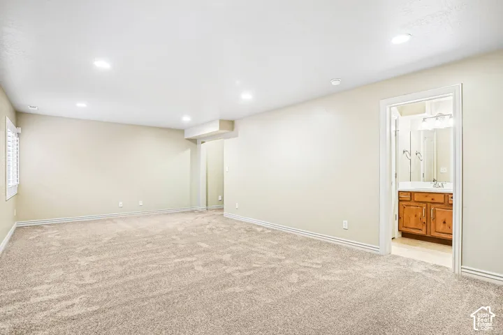 Recessed lighting, wall-to-wall carpeting, window with plantation shutters, and an adjacent bathroom featuring a wood-finish vanity with a built-in sink