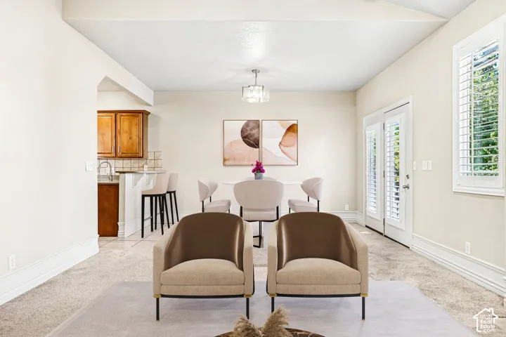 Vaulted ceiling with a contemporary chandelier, French doors with interior shutters, wall-to-wall carpeting, and wood cabinetry in the kitchen area