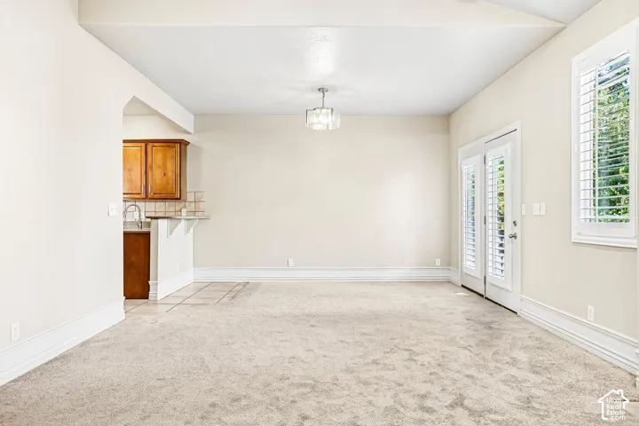 Vaulted ceiling, contemporary chandelier, French doors with louvered shutters, plantation shutters, and wood cabinetry with tile backsplash