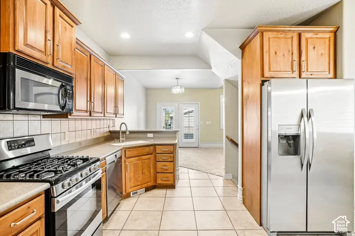 Kitchen featuring stainless steel appliances, wood cabinetry, tile flooring, and a tile backsplash