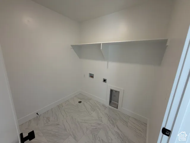 White walls with a single built-in shelf, marble-look tile flooring, and utility hookups