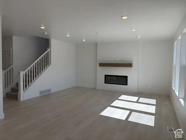 Open-concept living area featuring wood-finish flooring, a contemporary fireplace with a wood mantle, and recessed lighting