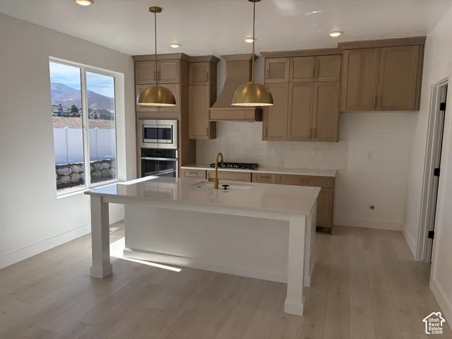 Kitchen featuring light wood-finish cabinetry, a white subway tile backsplash, stainless steel appliances, a center island with a white countertop, and recessed lighting