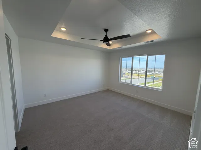 Recessed ceiling with integrated lighting, a ceiling fan, large windows, and neutral carpeting