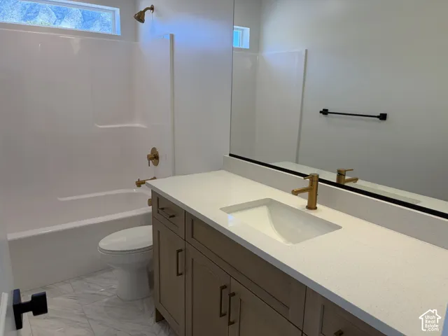 Vanity with integrated sink and brass-finish faucet, stone-look countertop, wood-finish cabinetry, and full-width mirror