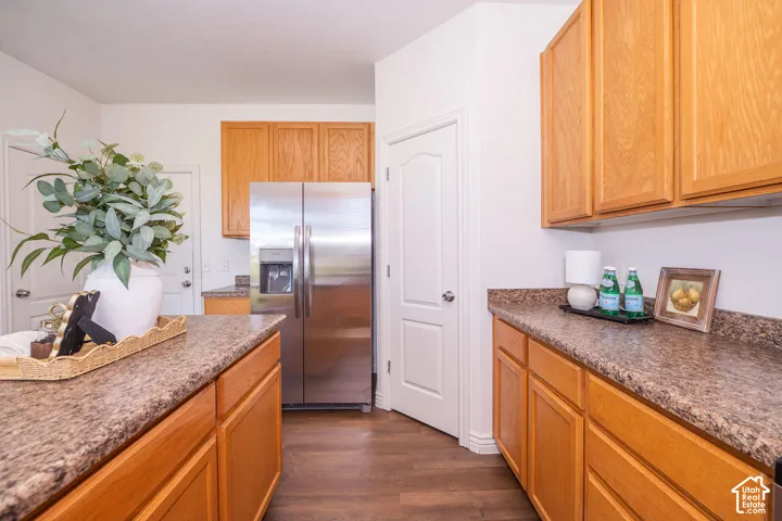 Wood-finish flooring complemented by granite-patterned countertops, natural wood cabinetry, and a stainless steel refrigerator with an external ice and water dispenser