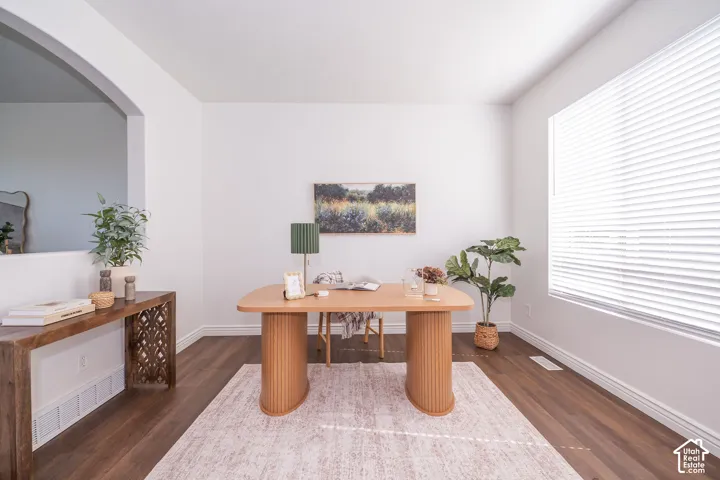 Hardwood-finish flooring throughout, bright white walls, large window with blinds, and an arched entry