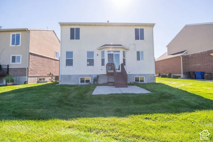 Expansive rear yard with a manicured lawn, concrete patio, and exterior stairs leading to a glass sliding door