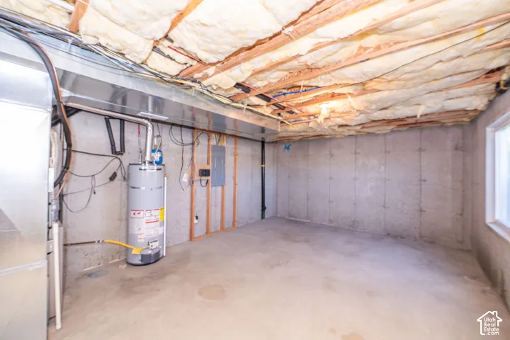 Unfinished concrete basement with exposed ceiling insulation, concrete walls, a water heater, and a window