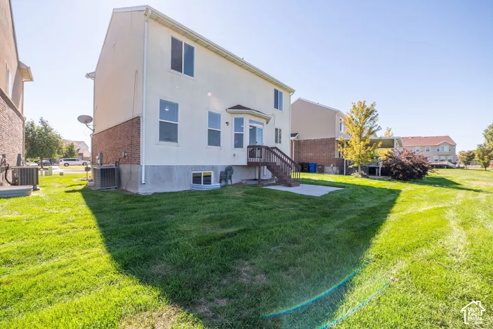 Expansive backyard featuring a manicured lawn, concrete patio, and a deck with stairs