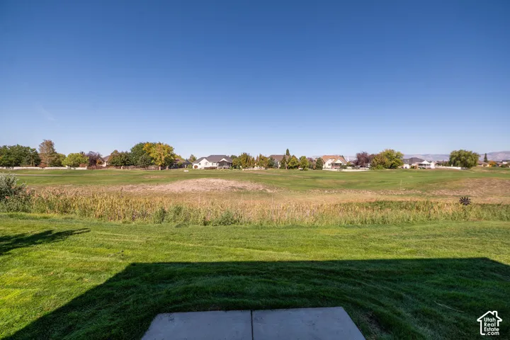 Expansive green space with distant residential properties, mature trees, and a clear sky