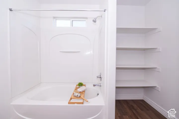 White bathtub with a built-in shower, an overhead window, and chrome fixtures
