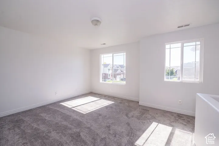 Neutral-toned carpeting, white walls, two window units, and a ceiling-mounted light fixture