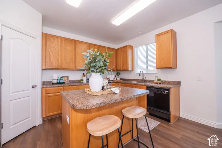 Wood-finish flooring, kitchen island with seating, natural wood cabinetry, dark-finish appliances, and a stainless steel sink with a pull-down faucet