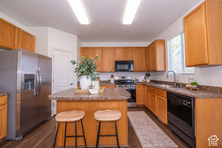 Kitchen featuring wood-finish flooring, a central island, light wood cabinetry, stainless steel refrigerator, and integrated sink