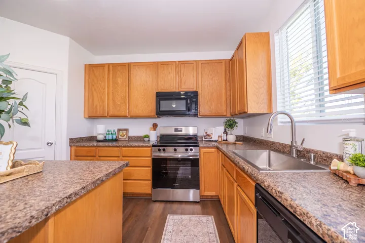 Kitchen featuring wood-finish cabinetry, stainless steel appliances, granite-look countertops, a stainless steel sink with a high-arc faucet, and wood-finish flooring