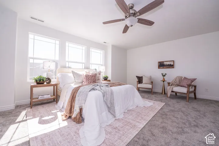 White walls, multiple windows, ceiling fan with light fixture, and gray carpeting
