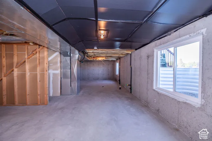 Unfinished basement with concrete flooring and exposed ceiling, featuring wood framing, exposed ductwork, and a window with a well