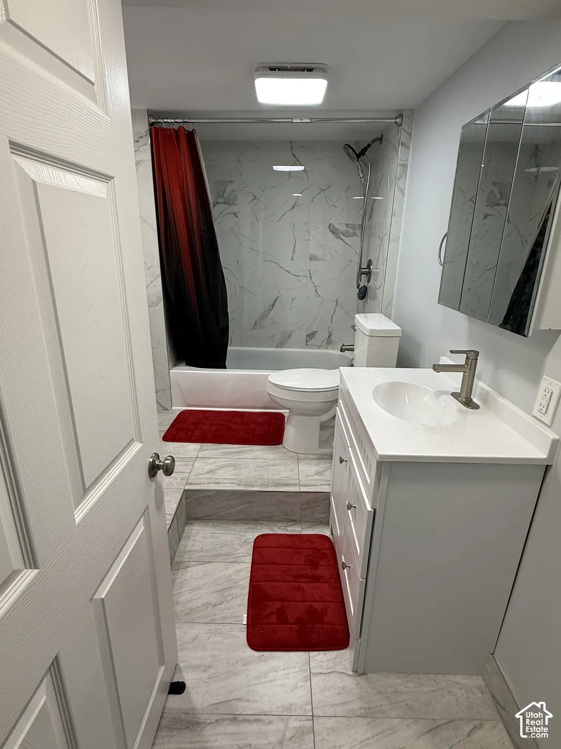 Bathroom featuring a white vanity with an integrated sink, a mirrored medicine cabinet, a bathtub with a shower system, and wall-mounted tile