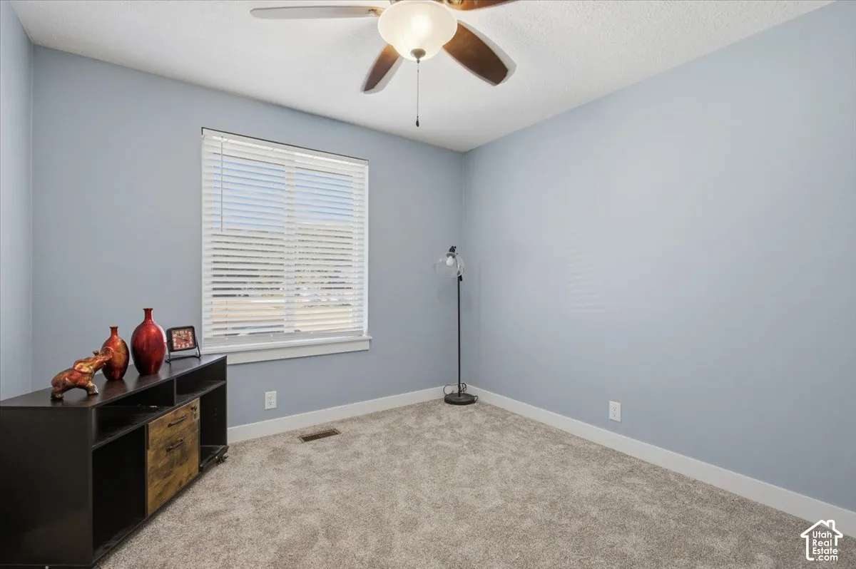 Light blue wall paint, window with blinds, ceiling fan, and carpeted flooring