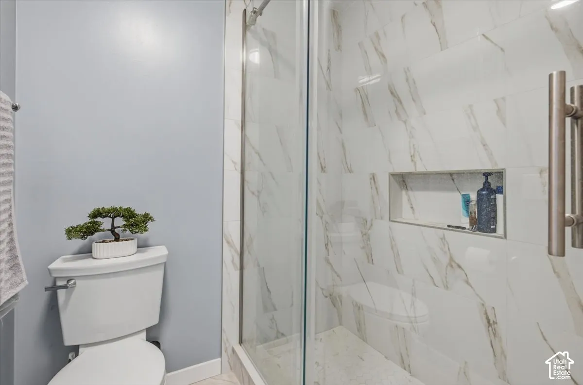 Glass-enclosed shower with a recessed niche, featuring white and gold-toned wall tiling and a mosaic tile floor