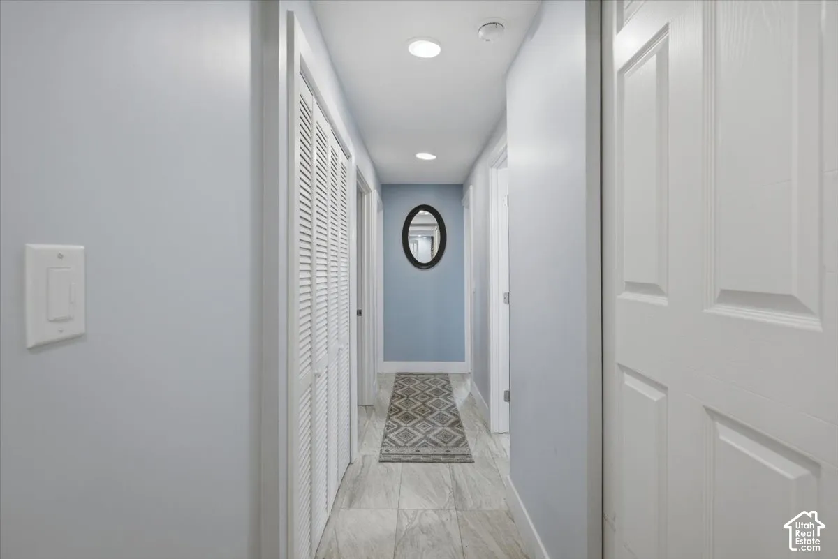 Recessed lighting illuminates the hallway, featuring wood-finish tile flooring and shutter-style closet doors