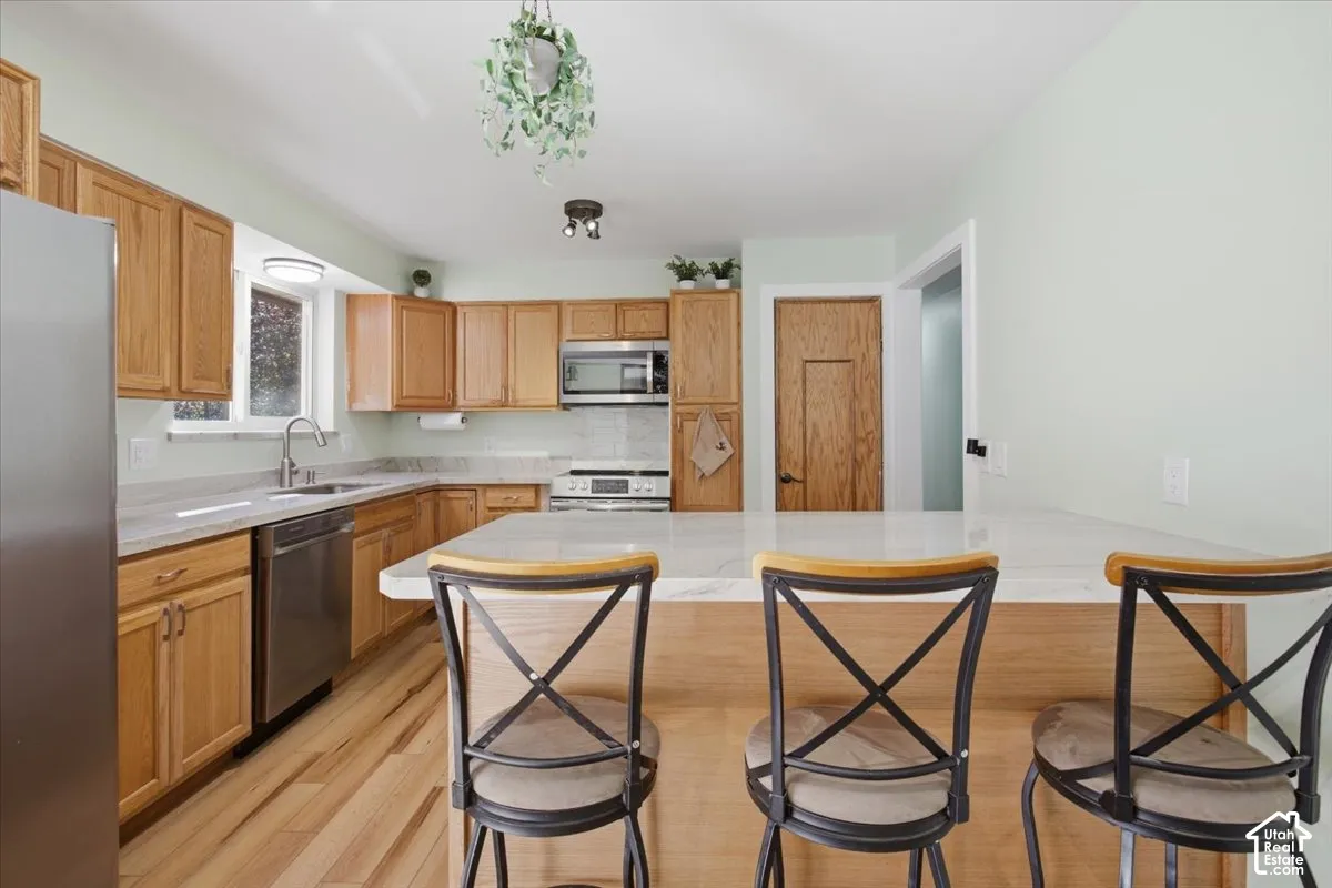 Kitchen featuring wood-finish cabinetry, stainless steel appliances, a white countertop, light wood-finish flooring, and a kitchen island with seating