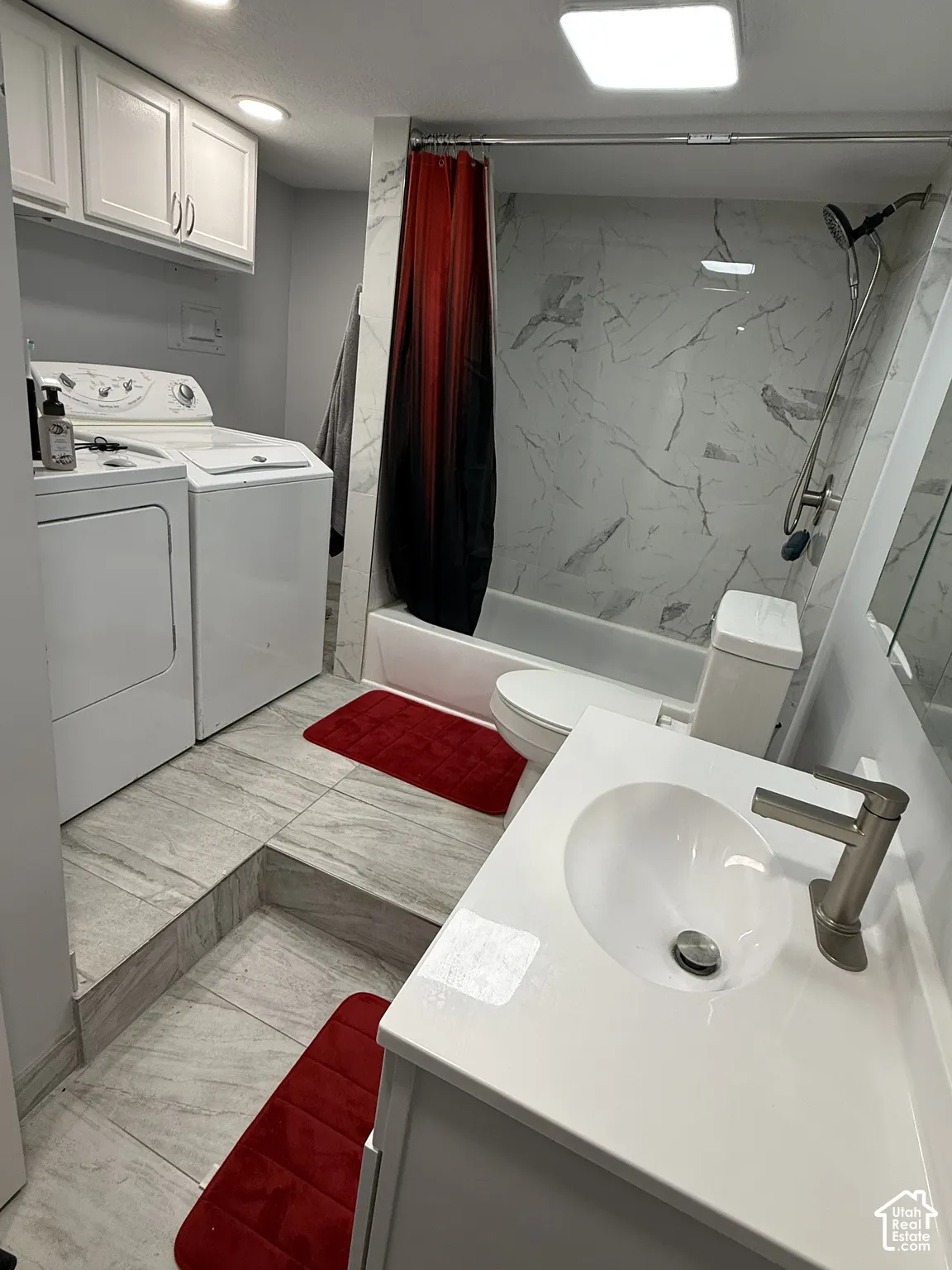 Integrated laundry appliances, full bathroom with tub/shower combination, vanity with single basin sink, wall-mounted mirror, and tile flooring