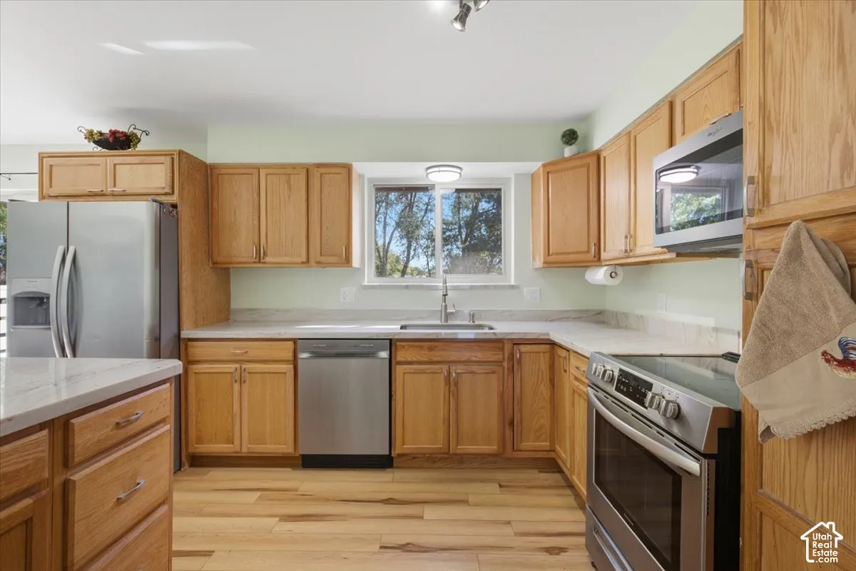 Kitchen featuring wood cabinetry, stainless steel appliances, light-toned countertops, wood-finish flooring, and a window above the sink